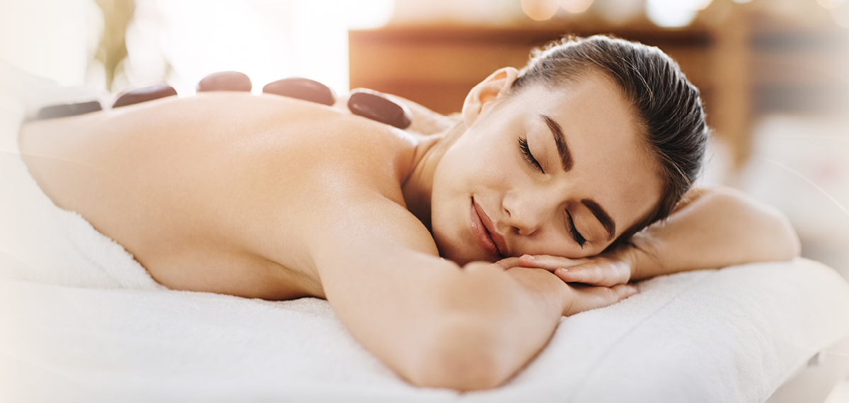 A person receiving a hot stone massage on their back in a calm spa setting.