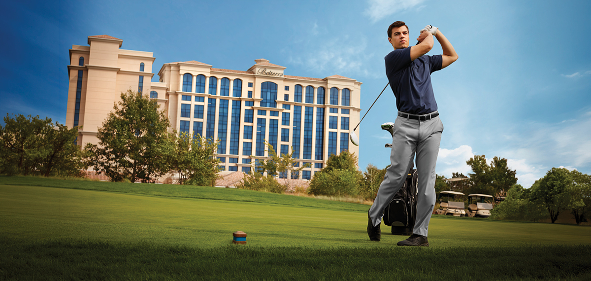 A golfer finishing a swing on a bright green course with the Belterra hotel rising in the background.
