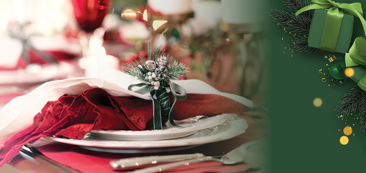 Holiday table setting with a red napkin, evergreen centerpiece, and festive green ornaments.