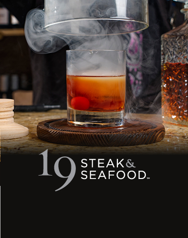 Smoked Old Fashioned cocktail with a cherry garnish under a glass cloche.