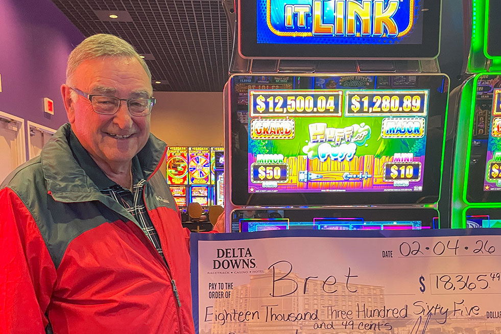 lucky winner in front of a slot machine with a check at delta downs