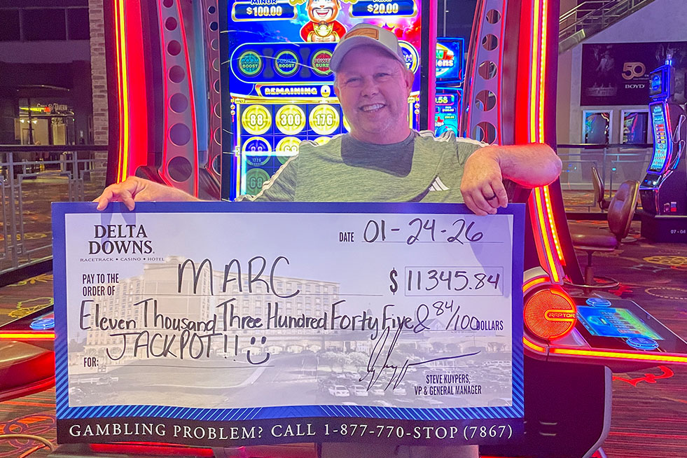 lucky winner in front of a slot machine with a check at delta downs