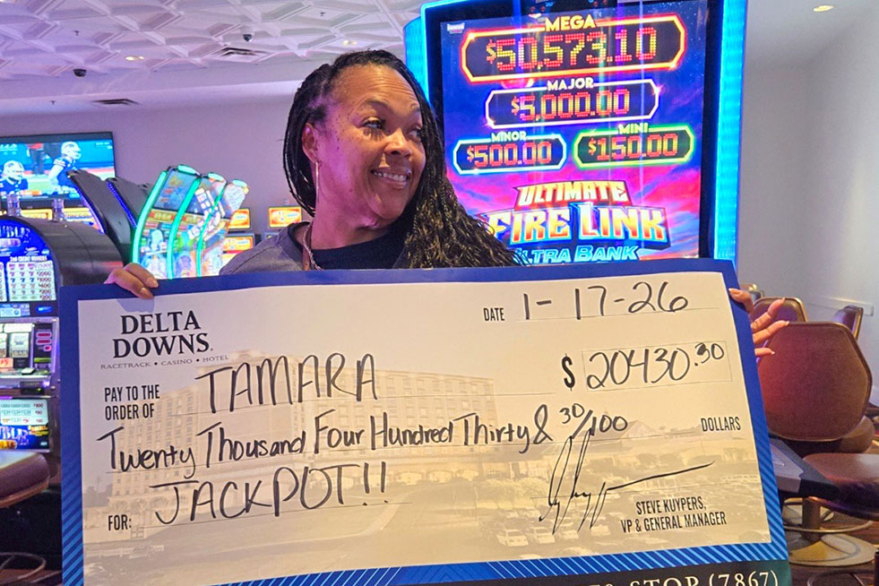 lucky winner in front of a slot machine with a check at delta downs