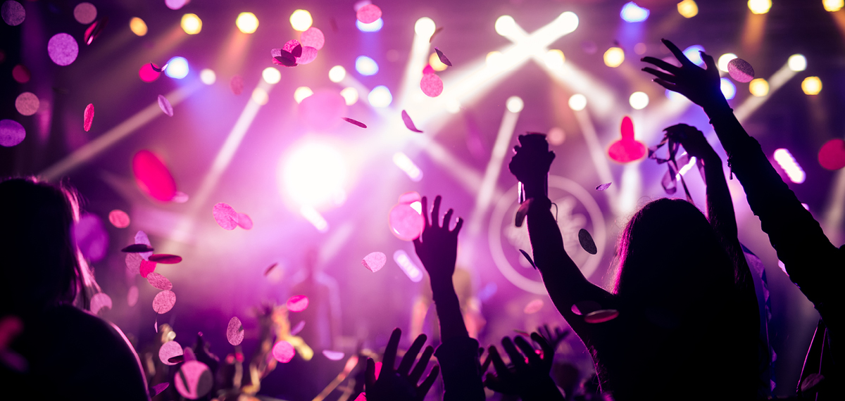 hands raised in the air at a concert with confetti and stage lights in the background