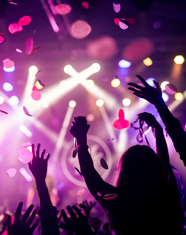 hands raised in the air at a concert with confetti and stage lights in the background
