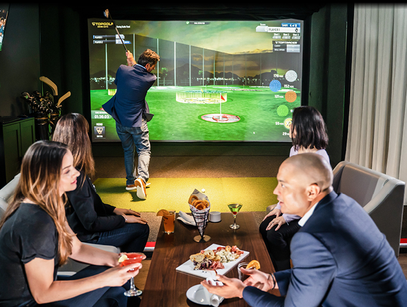 People enjoying conversation over cocktails and snacks while a man swings a golf club in the background