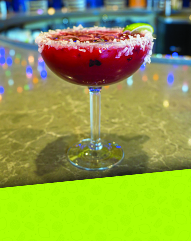 A blackberry coconut margarita garnished with fresh berries and coconut flakes.