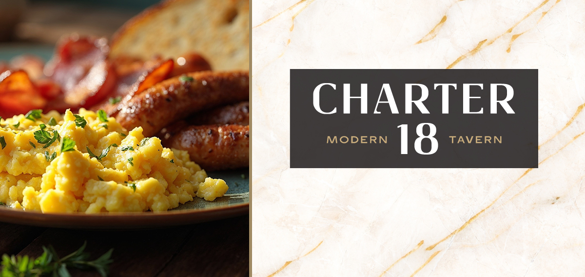 A plate of scrambled eggs, bacon, sausages, and toast on a wooden table with “Charter 18 Modern Tavern” below.
