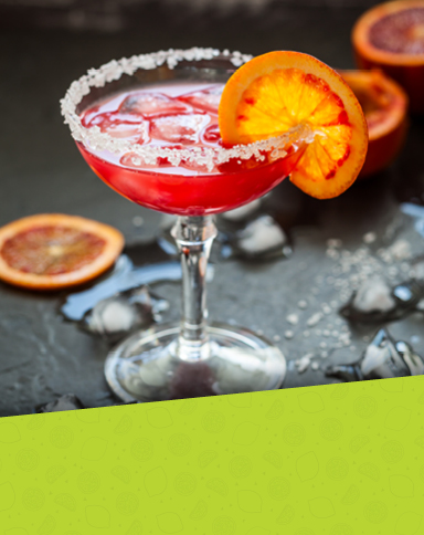 Red citrus cocktail in a salt-rimmed glass with ice and a blood orange garnish, surrounded by ice cubes and orange slices.