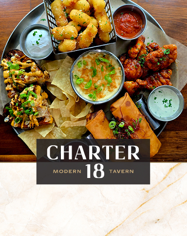 Charter 18 Modern Tavern appetizer platter with loaded nachos, cheese curds, chicken wings, dip and chips, and egg rolls.